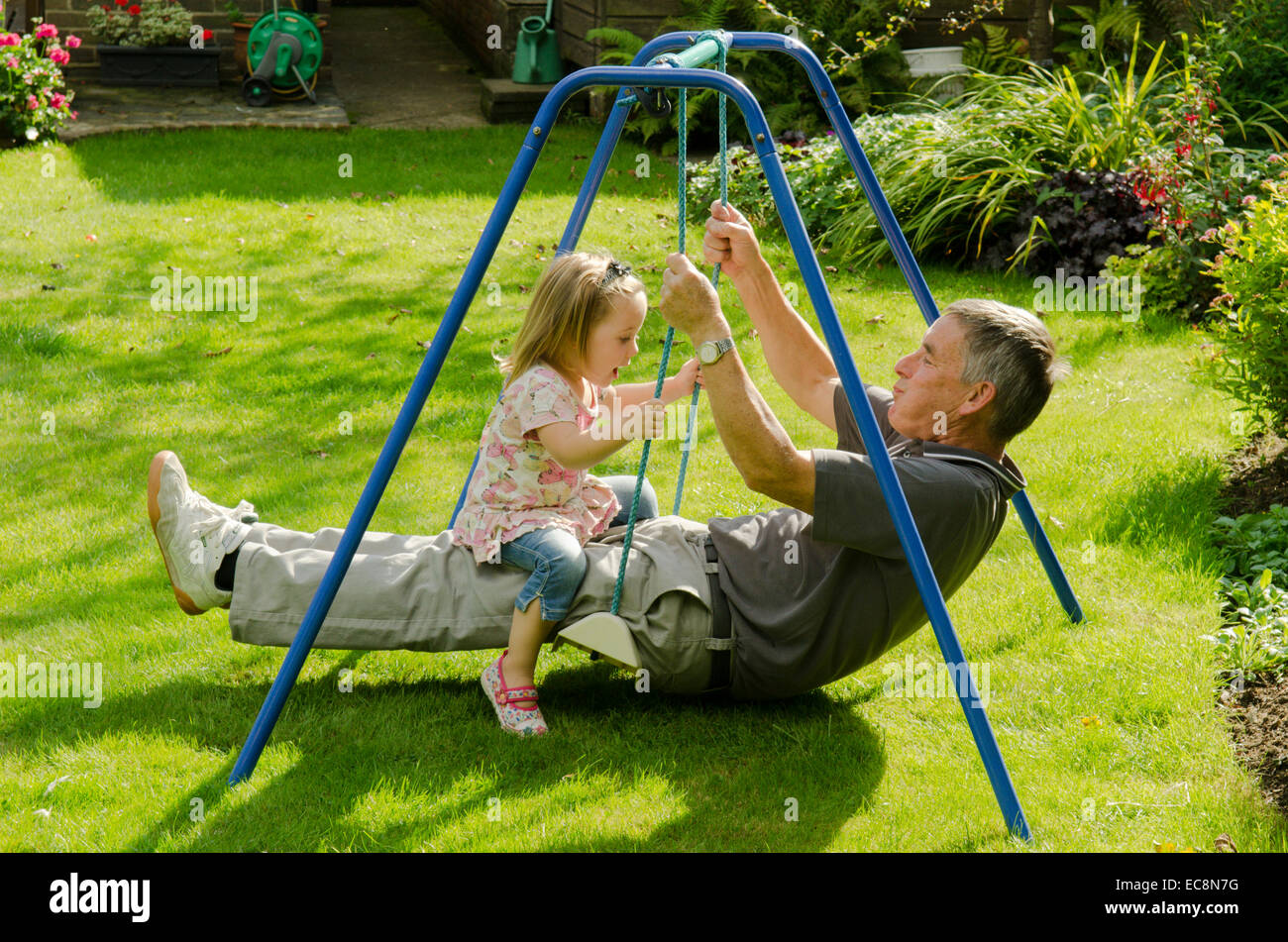 Nonno e nipote seduto su altalena in giardino. Inghilterra, Regno Unito. Settembre Foto Stock