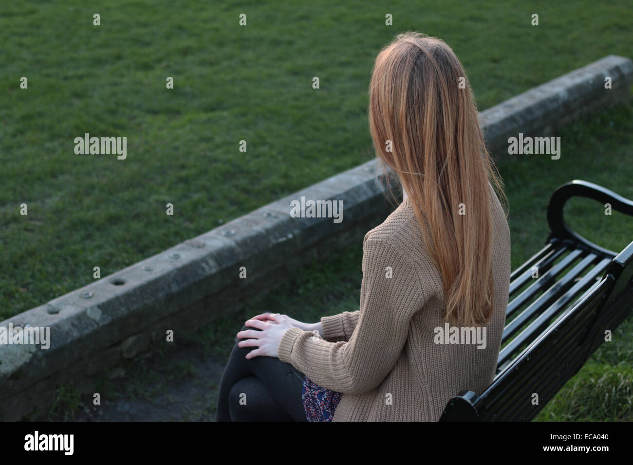 Vista posteriore del colpo di una giovane donna seduta su una panchina, guardando in lontananza. Foto Stock