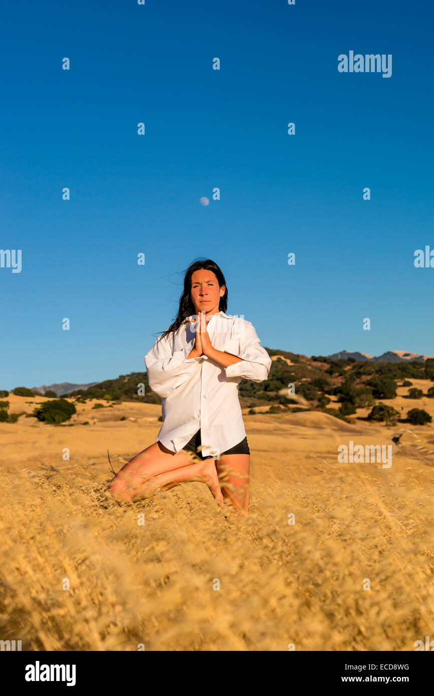 La donna in un yoga posa in un campo di erba dorata Foto Stock