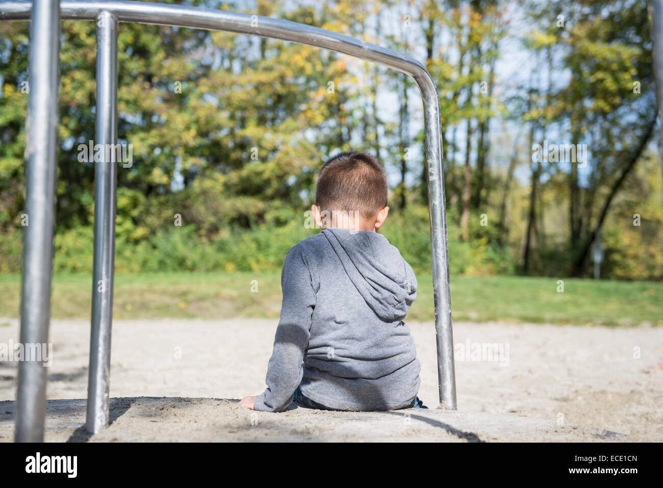 Piccolo ragazzo solitario seduto da solo nel parco giochi Foto Stock