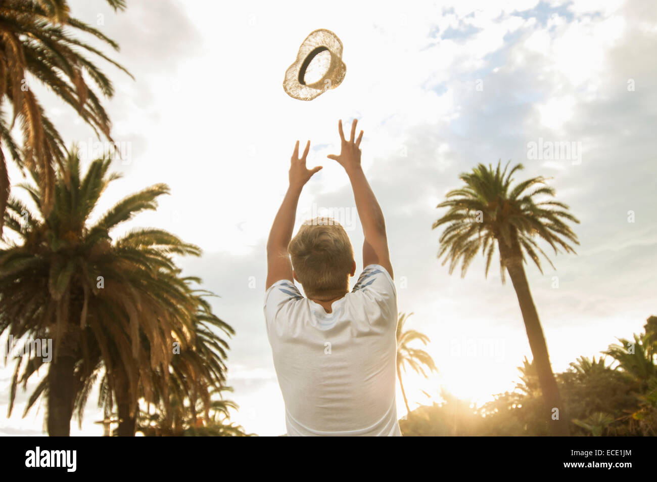 Ragazzo adolescente gettando hat in aria palme felice Foto Stock