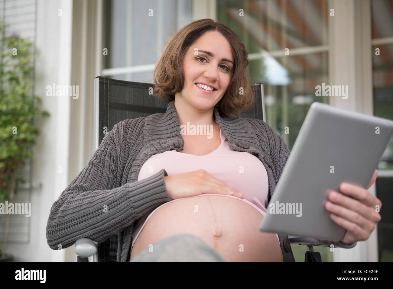 Donna incinta azienda computer tablet sorridente Foto Stock