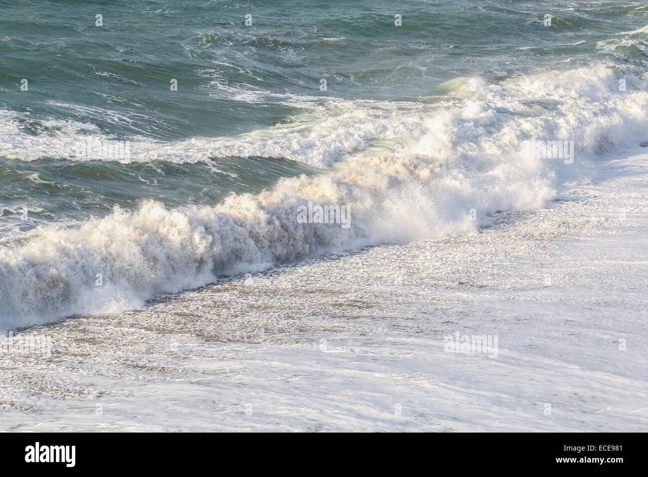Onde increspato in rotolamento su di una spiaggia di sabbia nel Regno Unito. Mare, spray e di acqua bianca sono illuminate dal sole di dicembre. Foto Stock
