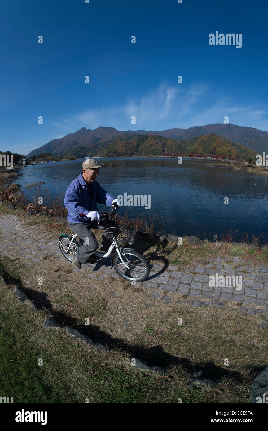 Un anziano uomo godendo di una bicicletta elettrica ride dalla riva del lago Kawaguchiko, Giappone. Foto Stock