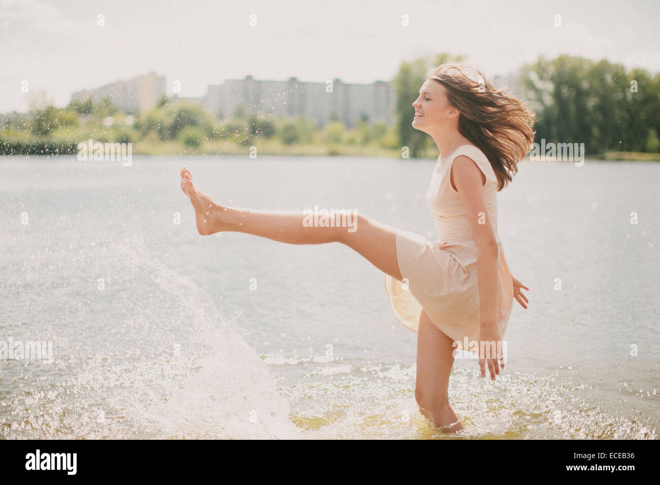 Ragazza adolescente in piedi in un fiume kicking acqua Foto Stock