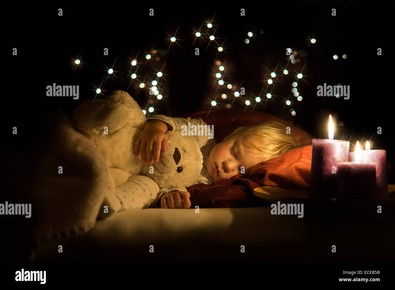 Candele accanto a un ragazzo addormentato coccolando un orsacchiotto Foto Stock