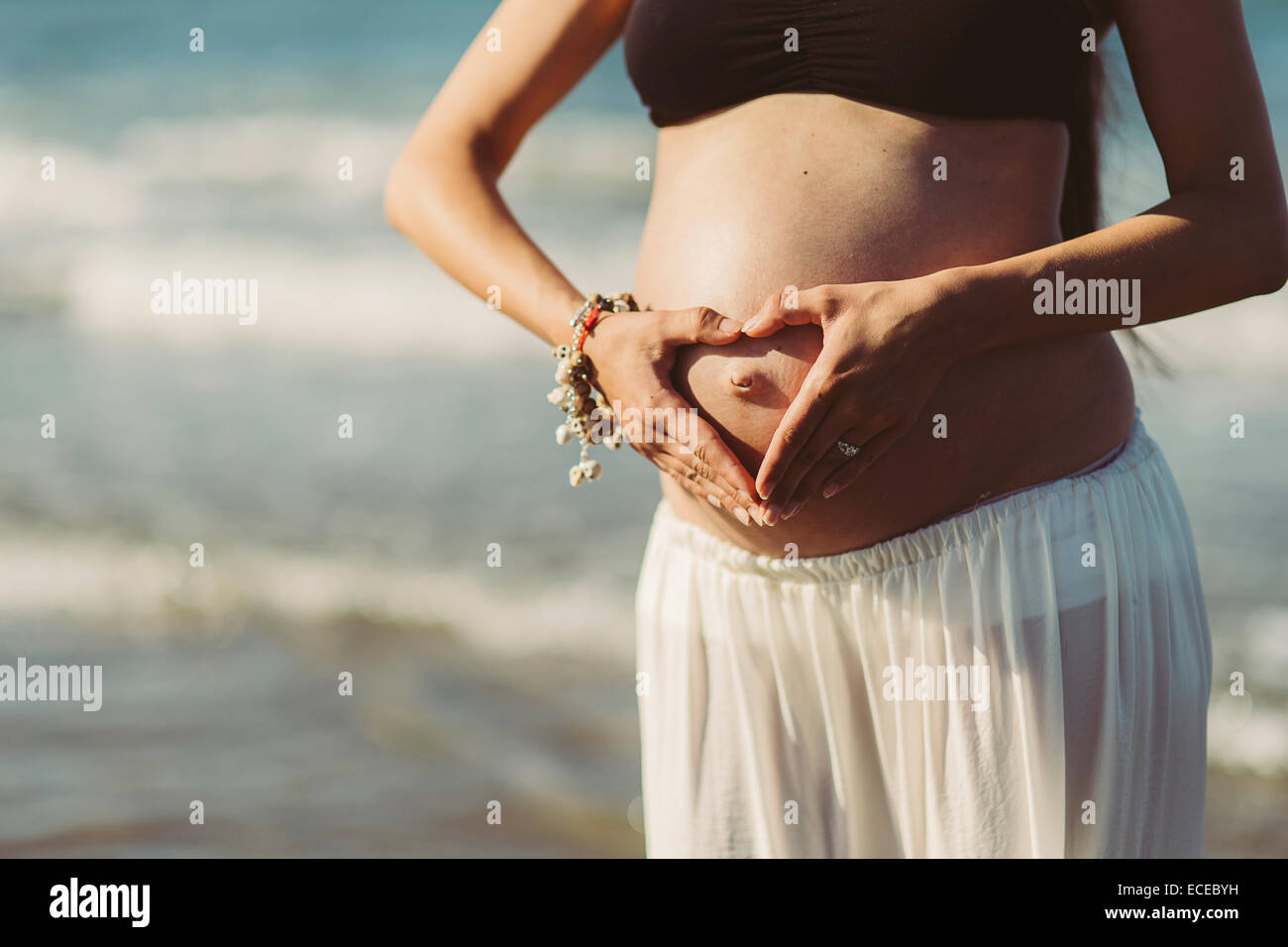 Donna incinta tenendo le mani a forma di cuore sul suo stomaco Foto Stock