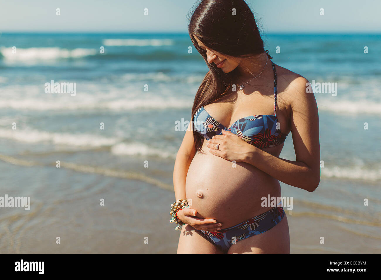 Giovane donna incinta permanente sulla spiaggia Foto Stock