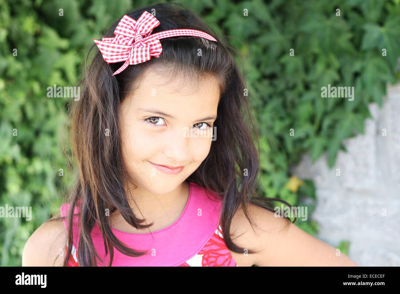 Dolce sorridente bambina (6-7) con lunghi capelli scuri sul verde sfondo edera Foto Stock