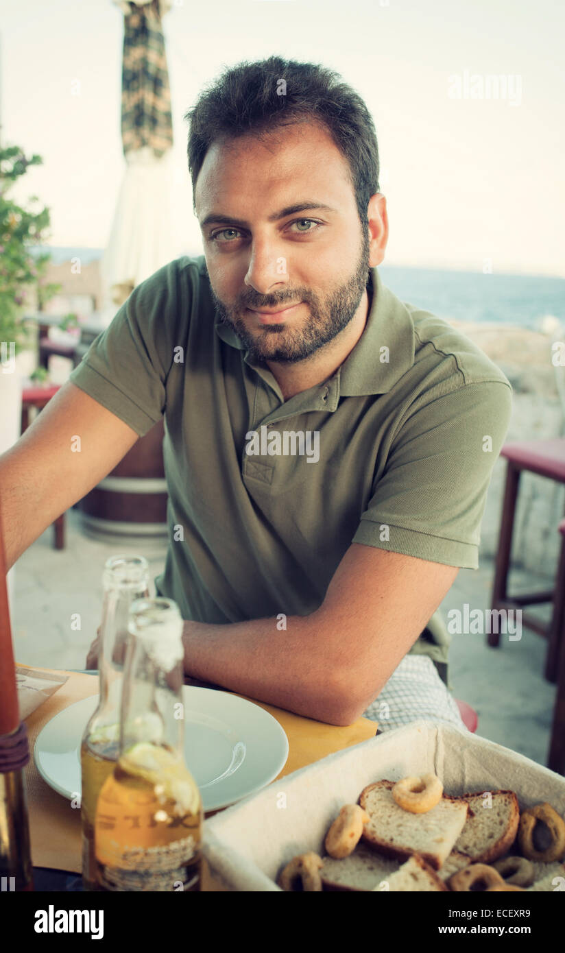 Giovane uomo gustando un drink seduti al ristorante vicino al mare. Foto Stock