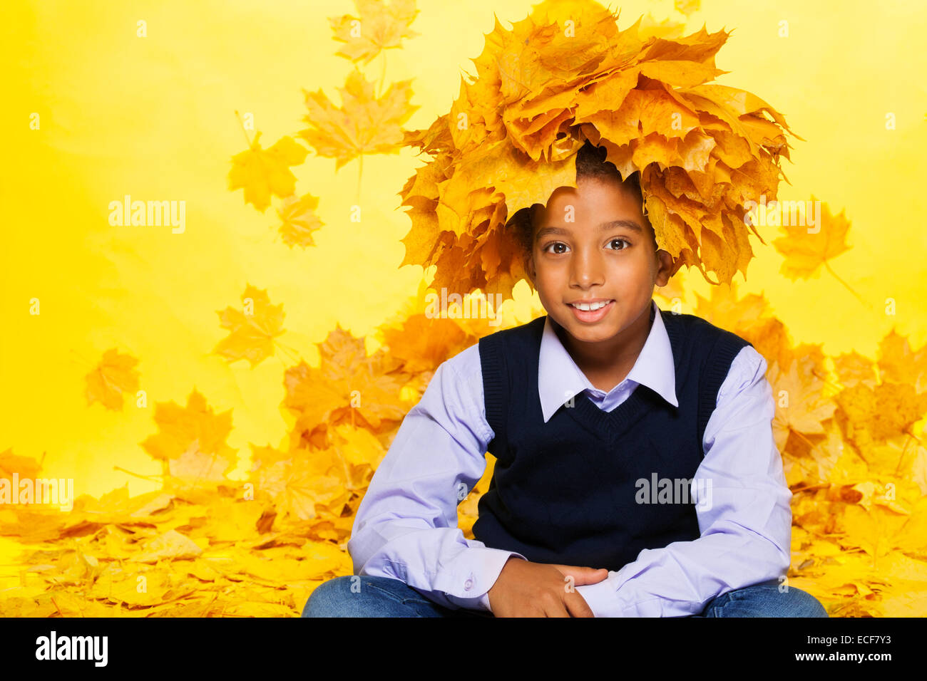 Felice ritratto di nero piccolo ragazzo indossa ghirlanda fatta di vivido arancione e giallo autunno foglie di acero Foto Stock