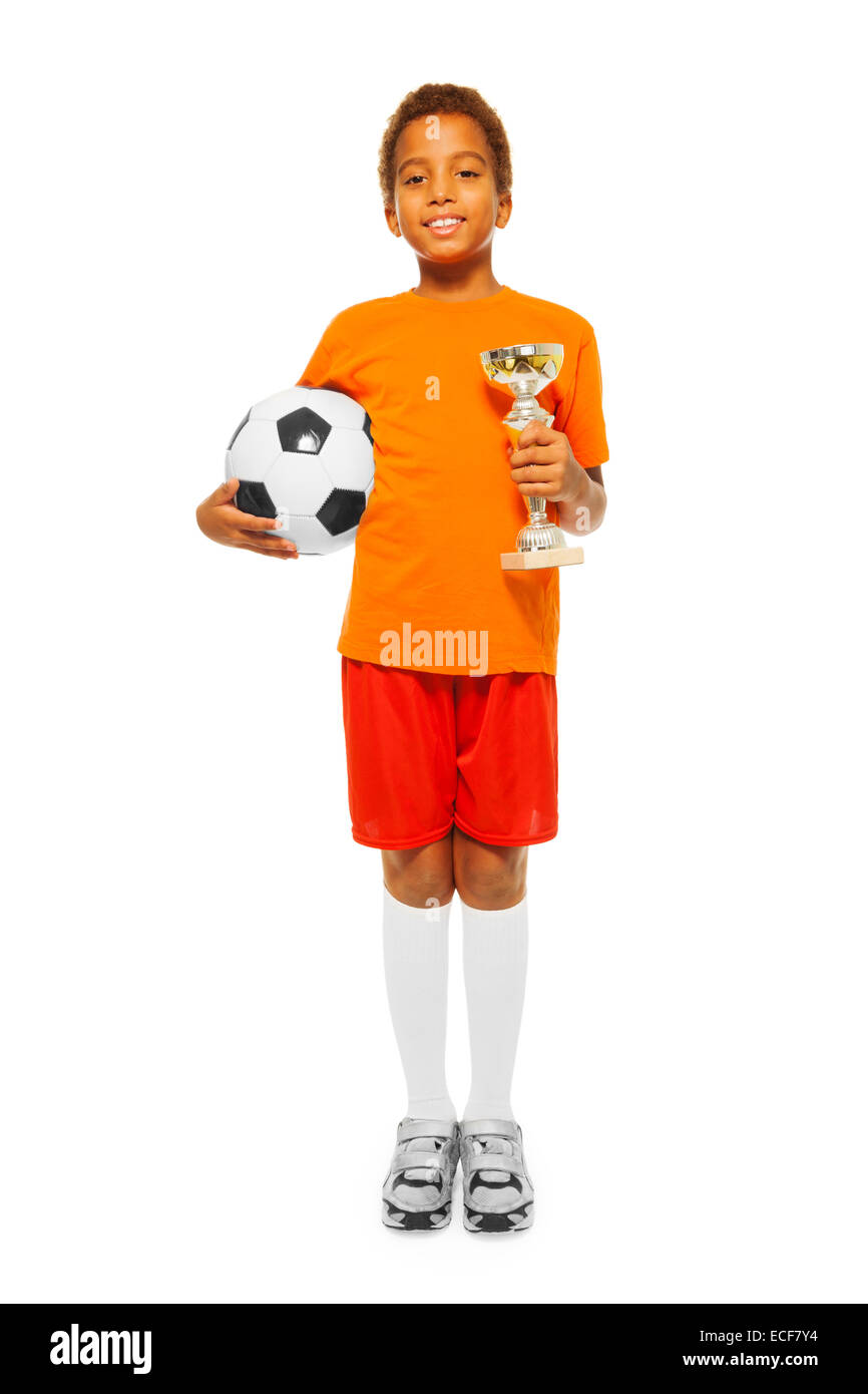 Felice African black boy con ricci capelli corti tenendo palla calcio e vincitori premio cup indossando sport team uniforme isol permanente Foto Stock