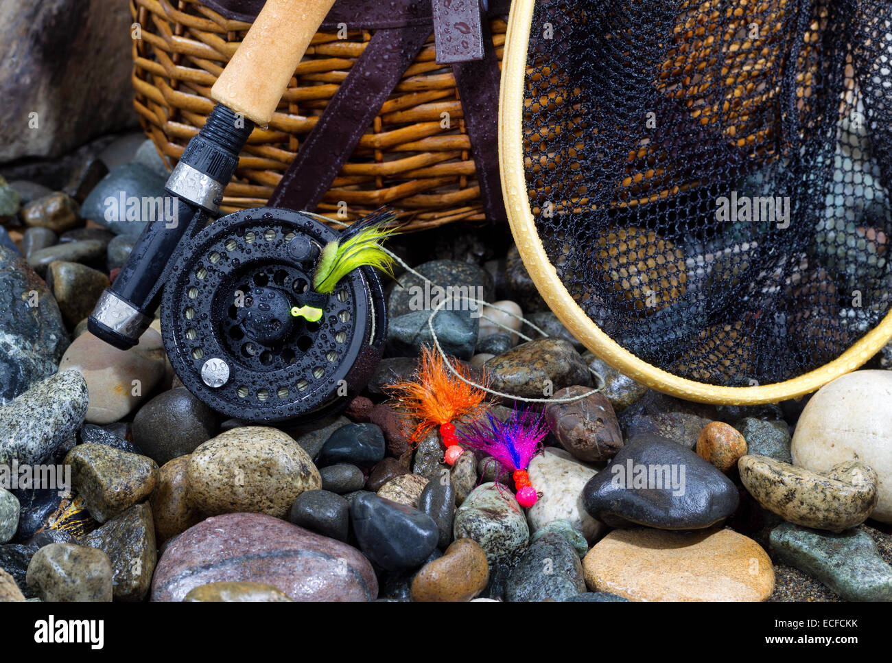 Primo piano della pesca fly aspo, landing net, cantra e assortita vola sul bagnato il letto del fiume pietre Foto Stock