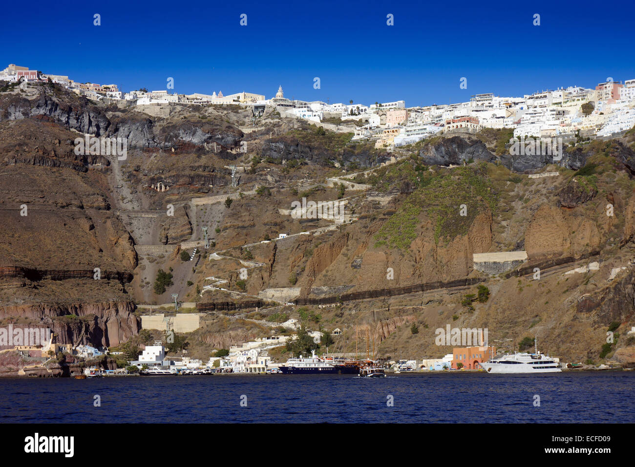 Case bianche dal mare blu sul bordo della caldera, il cratere vulcanico, Santorini con barche ormeggiate e a zig-zag percorso di asino Foto Stock