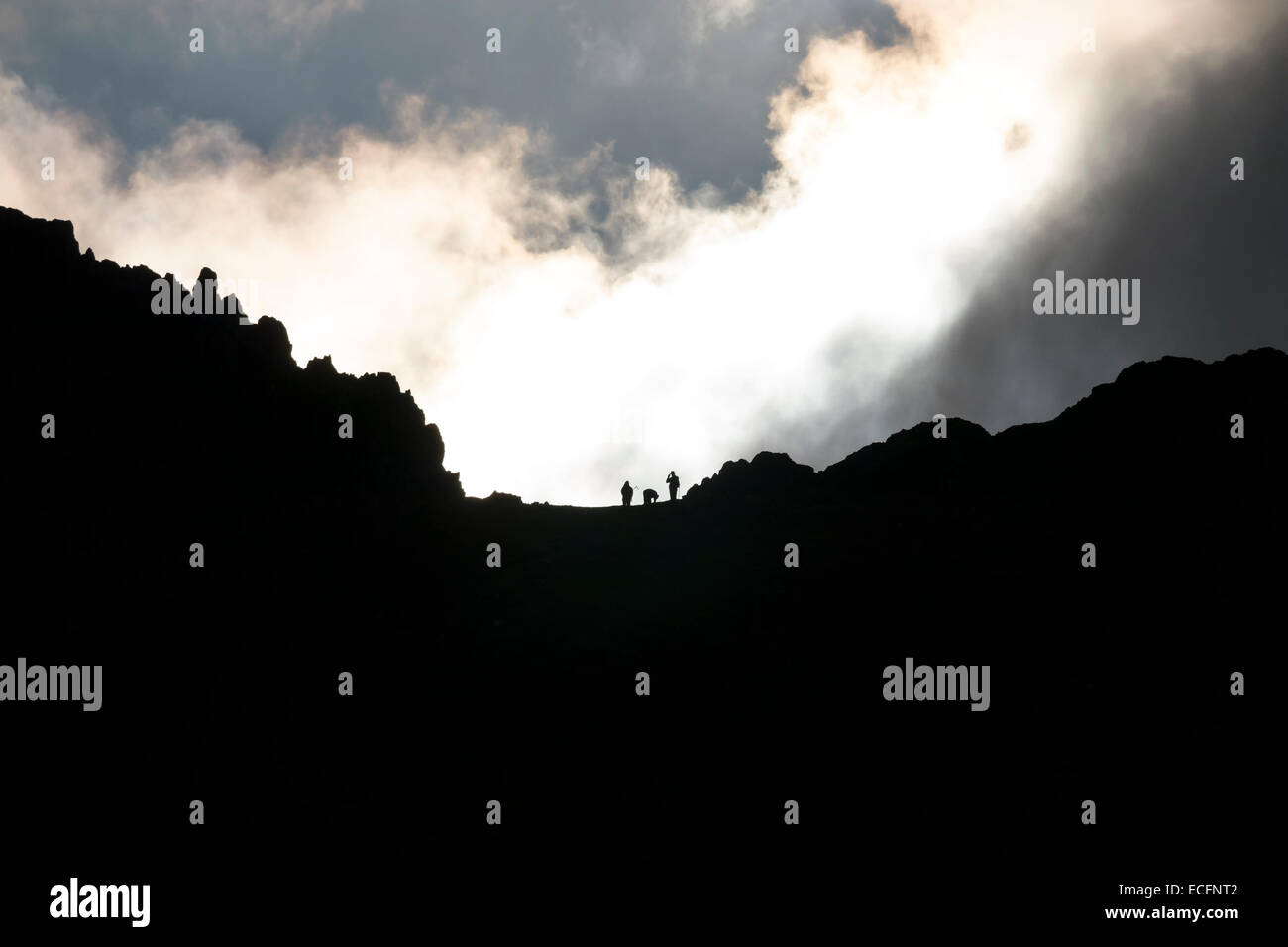Silhouette di tre walkers sul bordo di estensione montagna cresta, Helvellyn, Lake District, Cumbria, England, Regno Unito Foto Stock