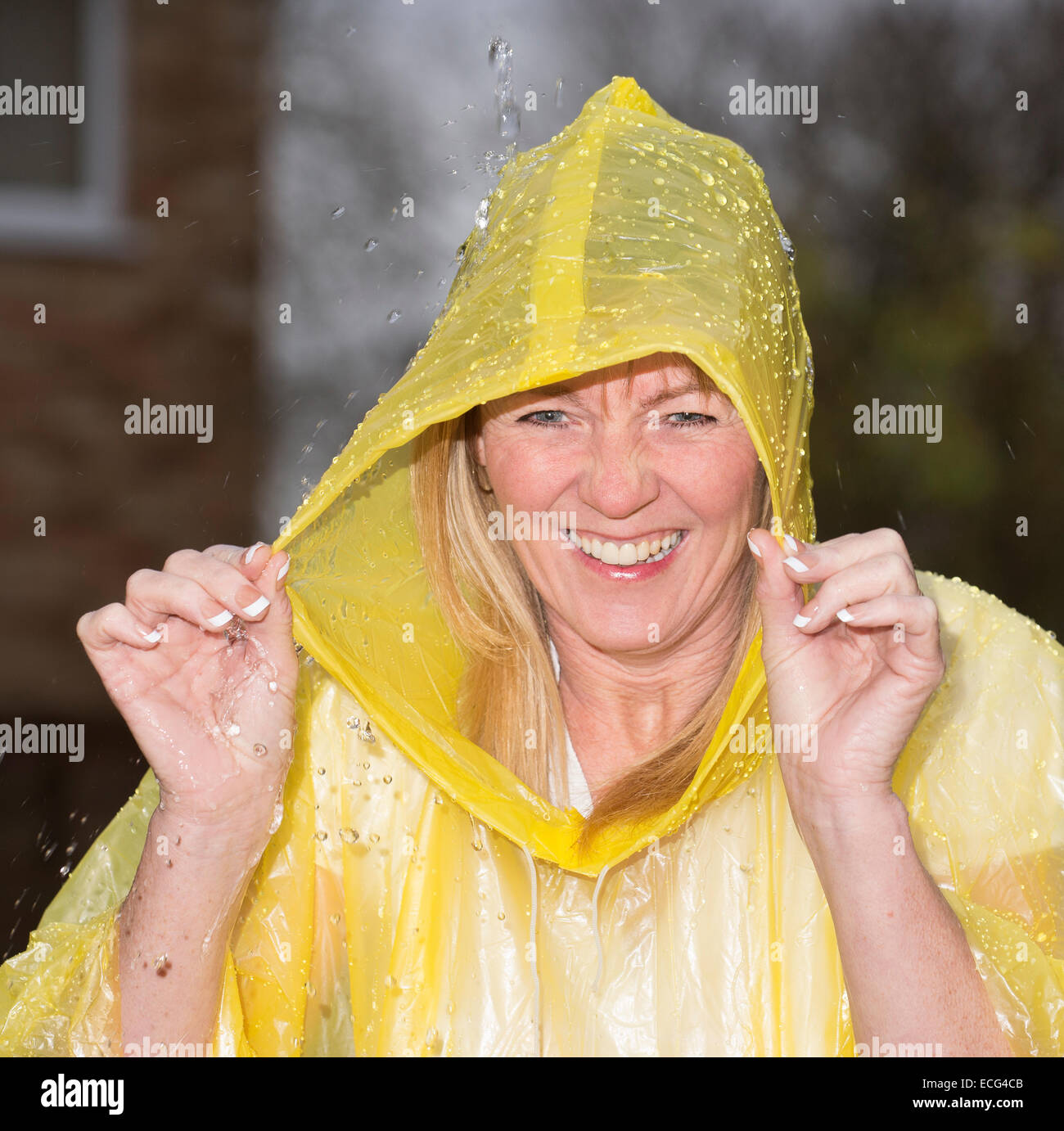 Donna che ride indossando un poncho di plastica durante una doccia di pioggia Foto Stock