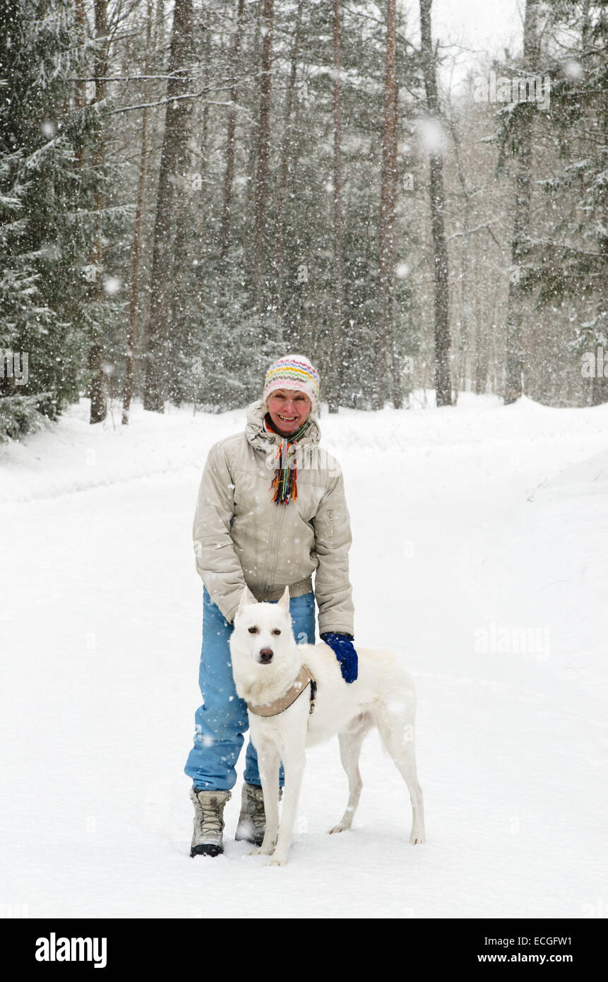 Donna con un cane in una passeggiata nel bosco durante una nevicata Foto Stock