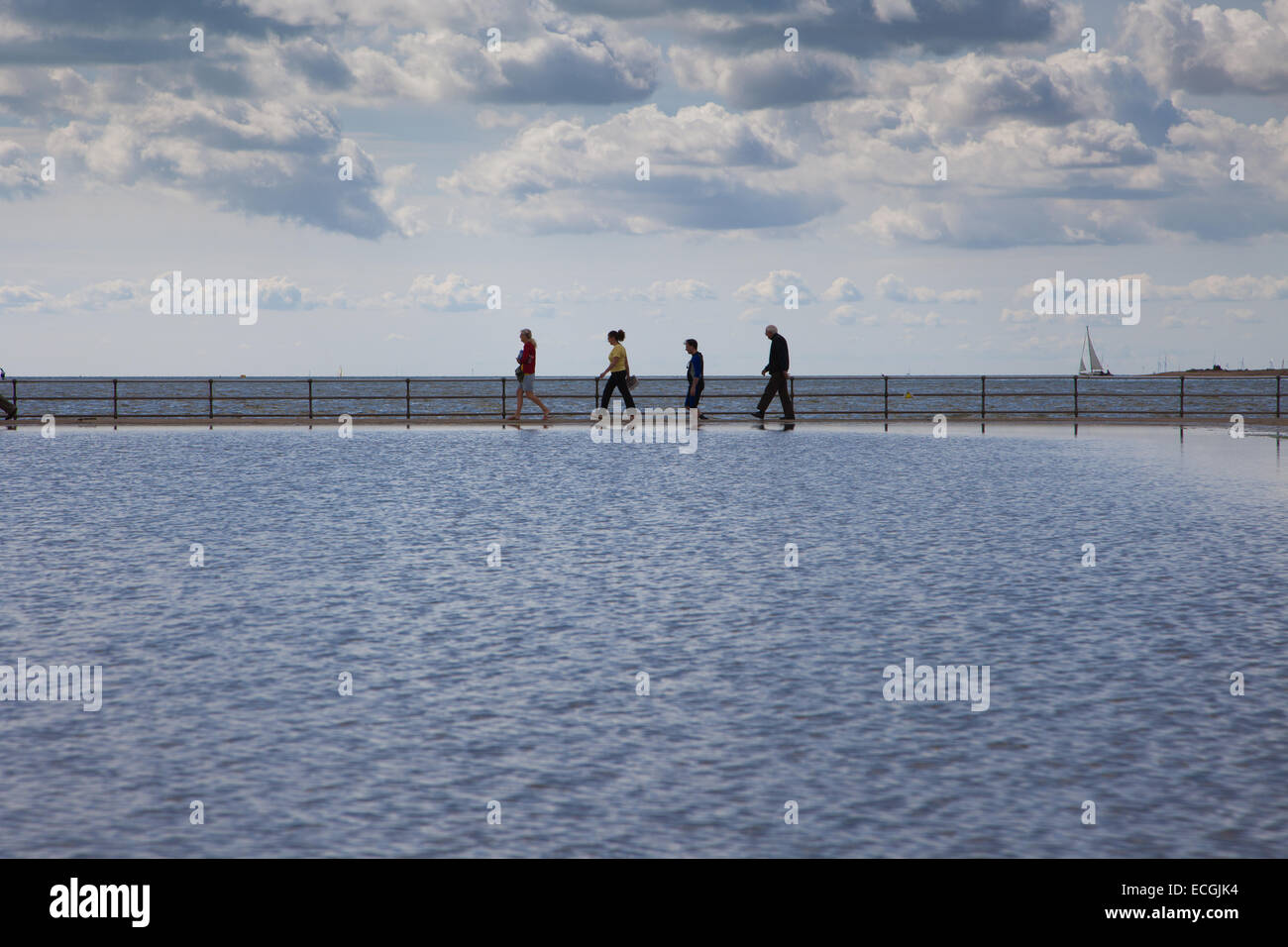 Le persone in vacanza al Brightlingsea oltrepassando la parete di marea con una grande area di cielo Foto Stock