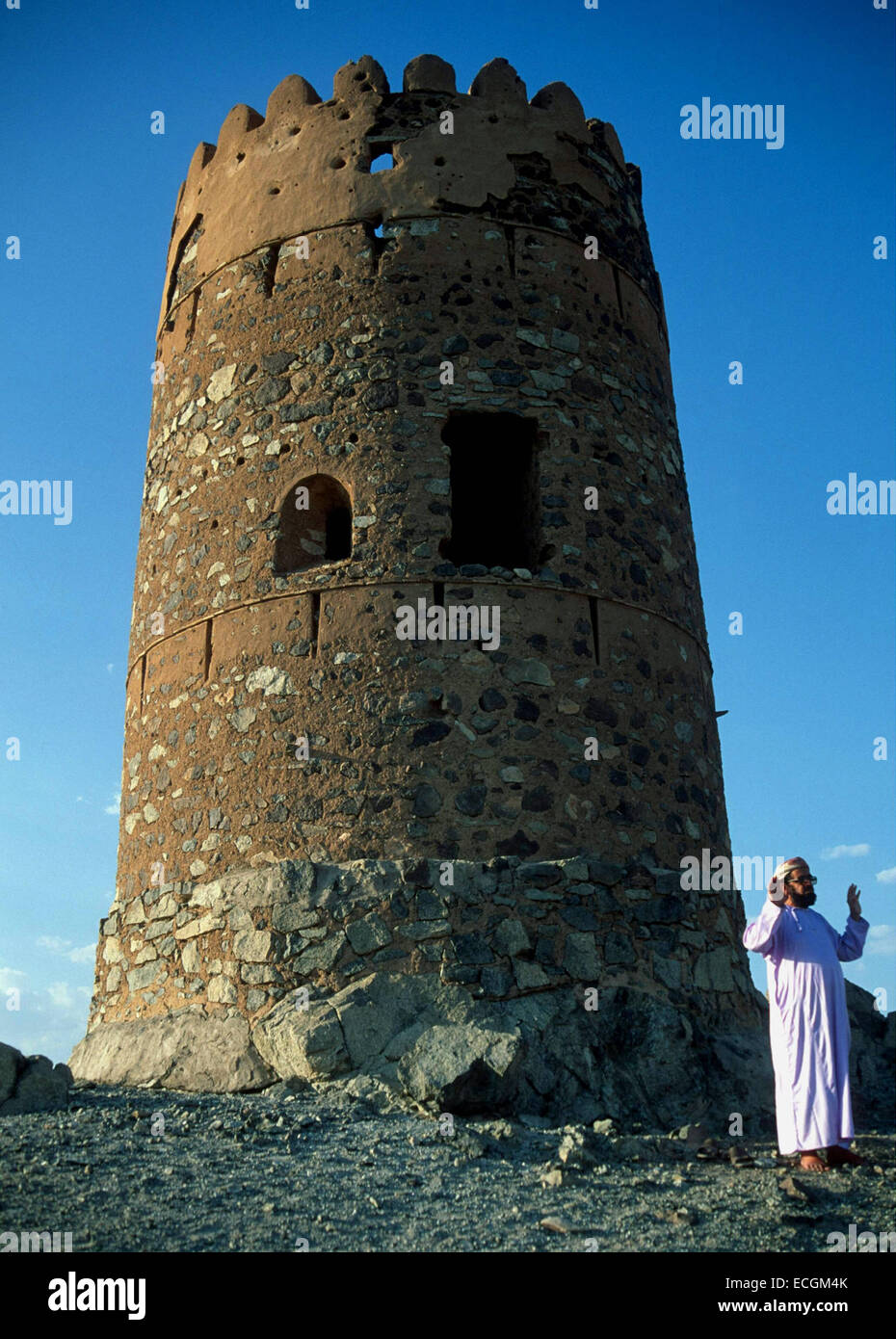Uomo musulmano prega accanto a una vecchia torre di avvistamento vicino al Mudayrib, cittadina sulle antiche vie carovaniere in Oman Foto Stock