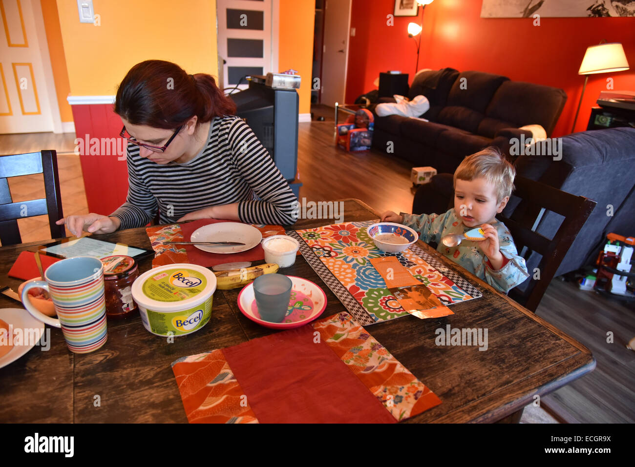 Una madre ignorando il suo bambino la lettura di un ipad al tavolo della colazione Foto Stock