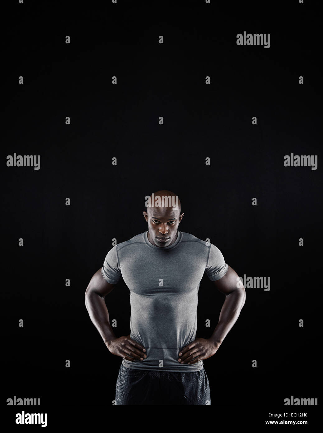Ritratto di giovane muscolare uomo in abbigliamento sportivo a fissare la fotocamera su sfondo nero. Atleta africana con le mani sui fianchi Foto Stock