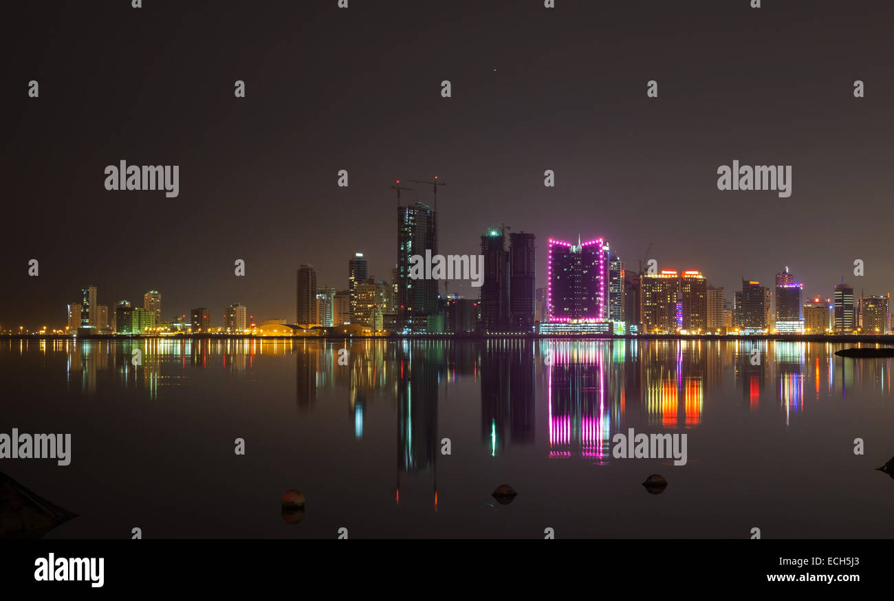 Notte moderno skyline della città con brillanti luci e riflessi nell'acqua. Manama, la capitale del Regno del Bahrain, Medio Oriente Foto Stock