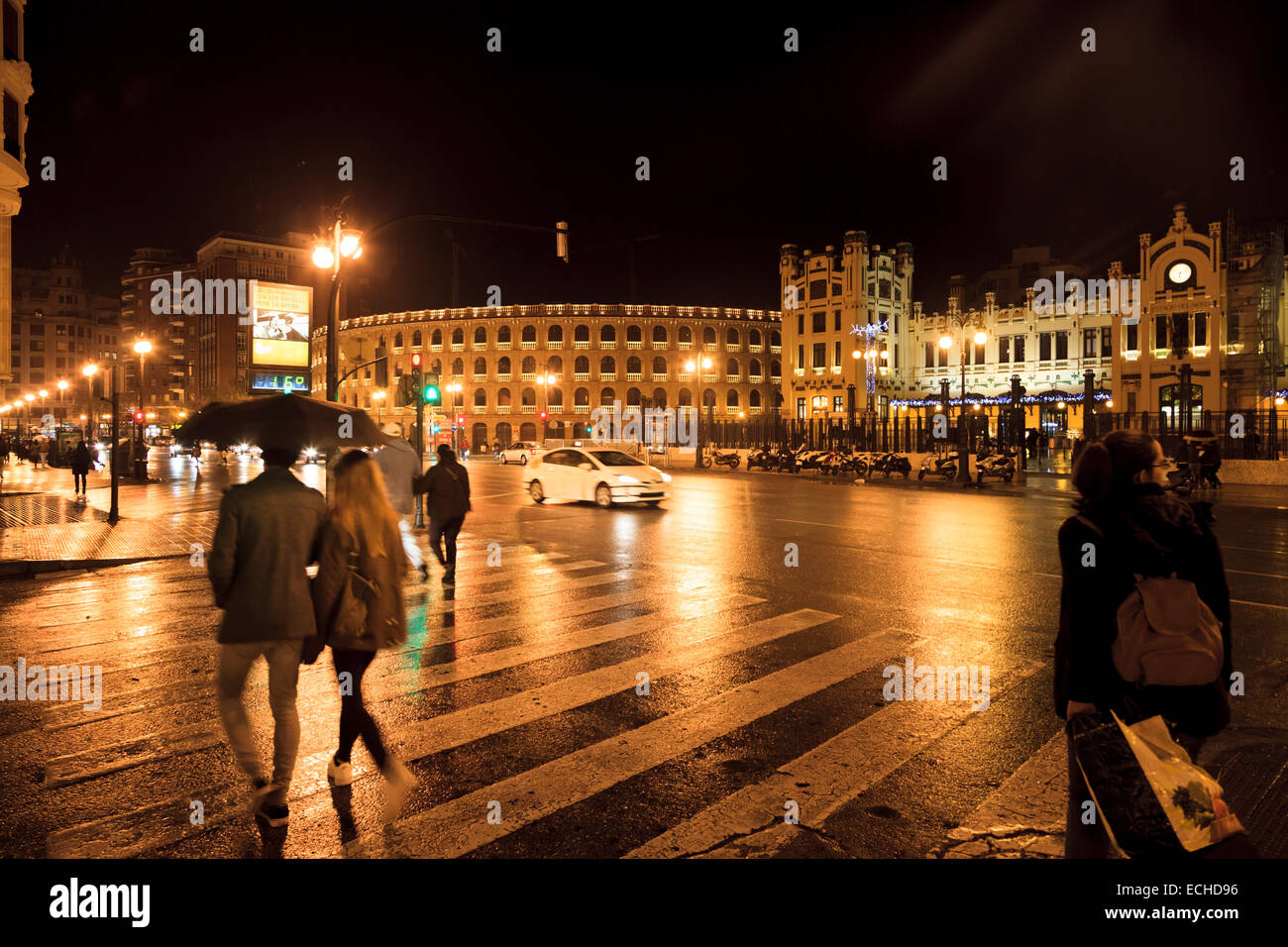 Le persone sotto gli ombrelloni su una notte piovosa sulle strade di Valencia in Spagna su un attraversamento pedonale Foto Stock