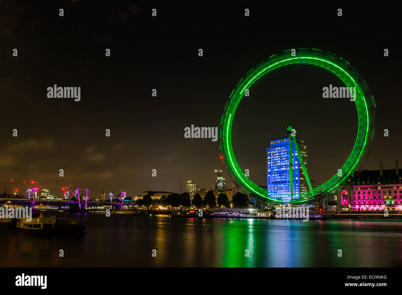 Una fotografia del London Eye sul Tamigi. Luci verdi riflettendo in acqua di notte tempo. Foto Stock