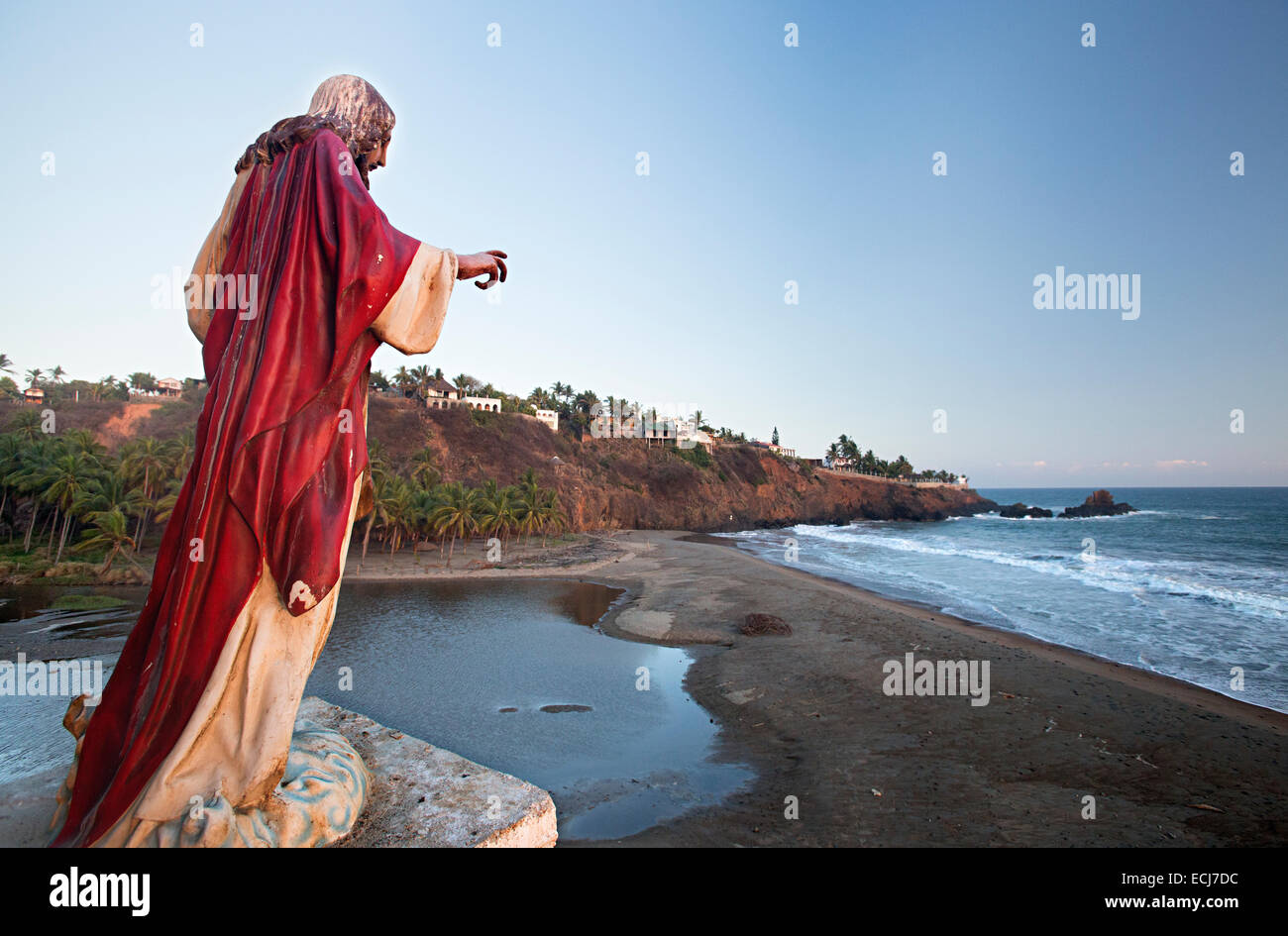 Statua di Gesù indossa mantello rosso si affaccia su di una spiaggia e piccola città. Foto Stock