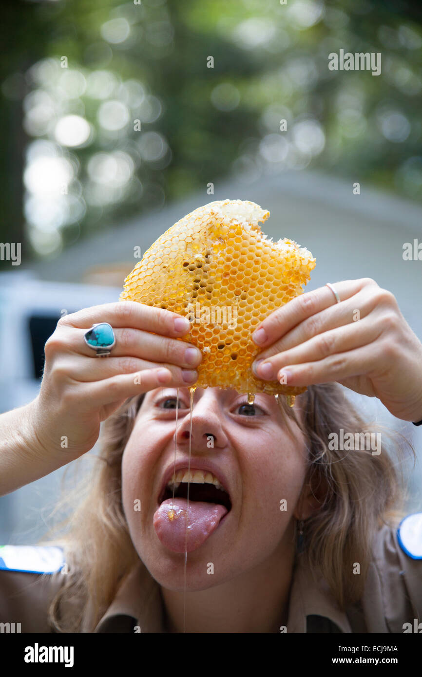 Una giovane donna mangia miele fresco come lei spreme fuori del nido d'ape. Foto Stock