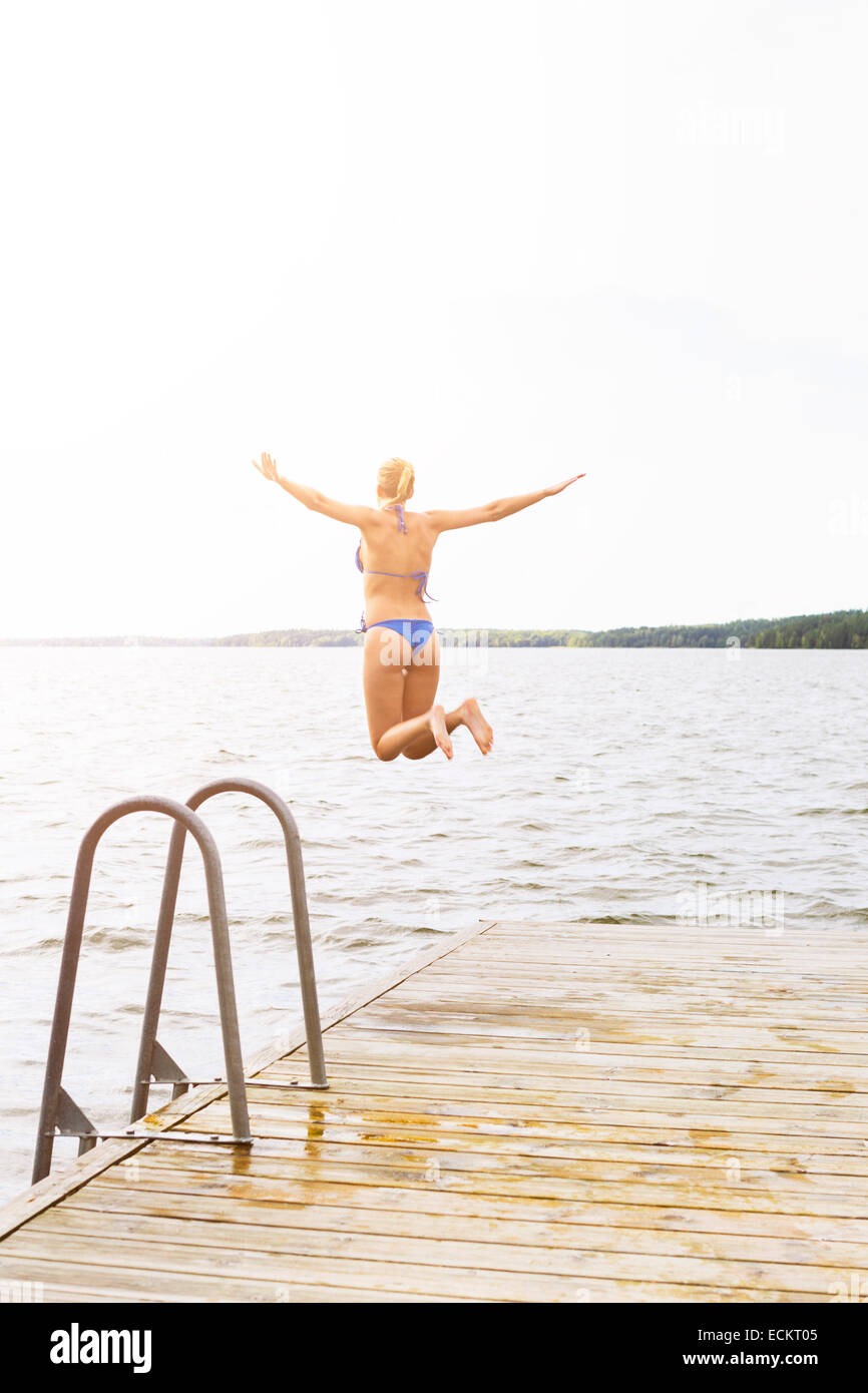 Vista posteriore della donna con le braccia aperte saltando nel lago Foto Stock