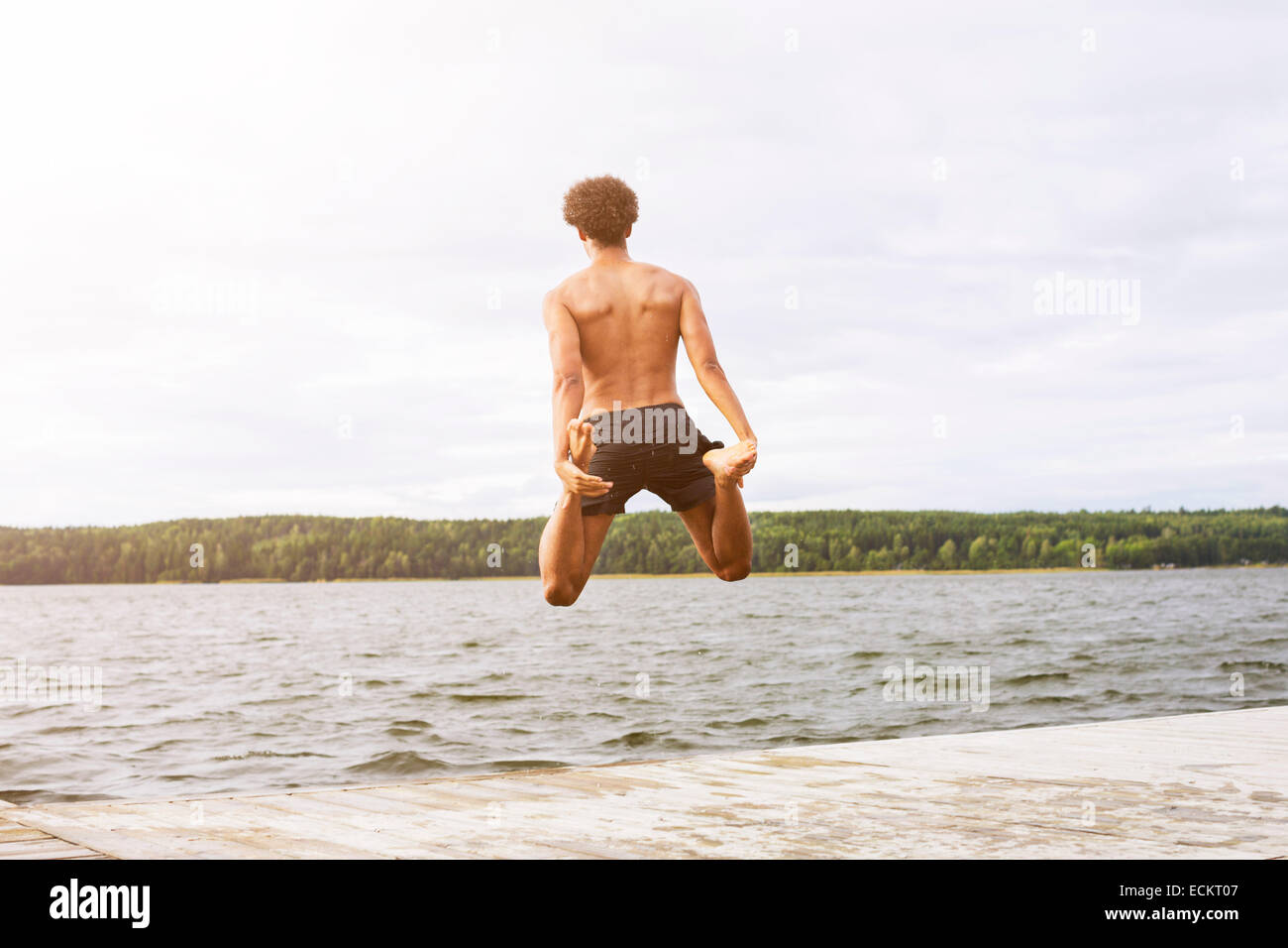 Lunghezza piena vista posteriore dell'uomo tenendo le gambe durante il salto nel lago Foto Stock