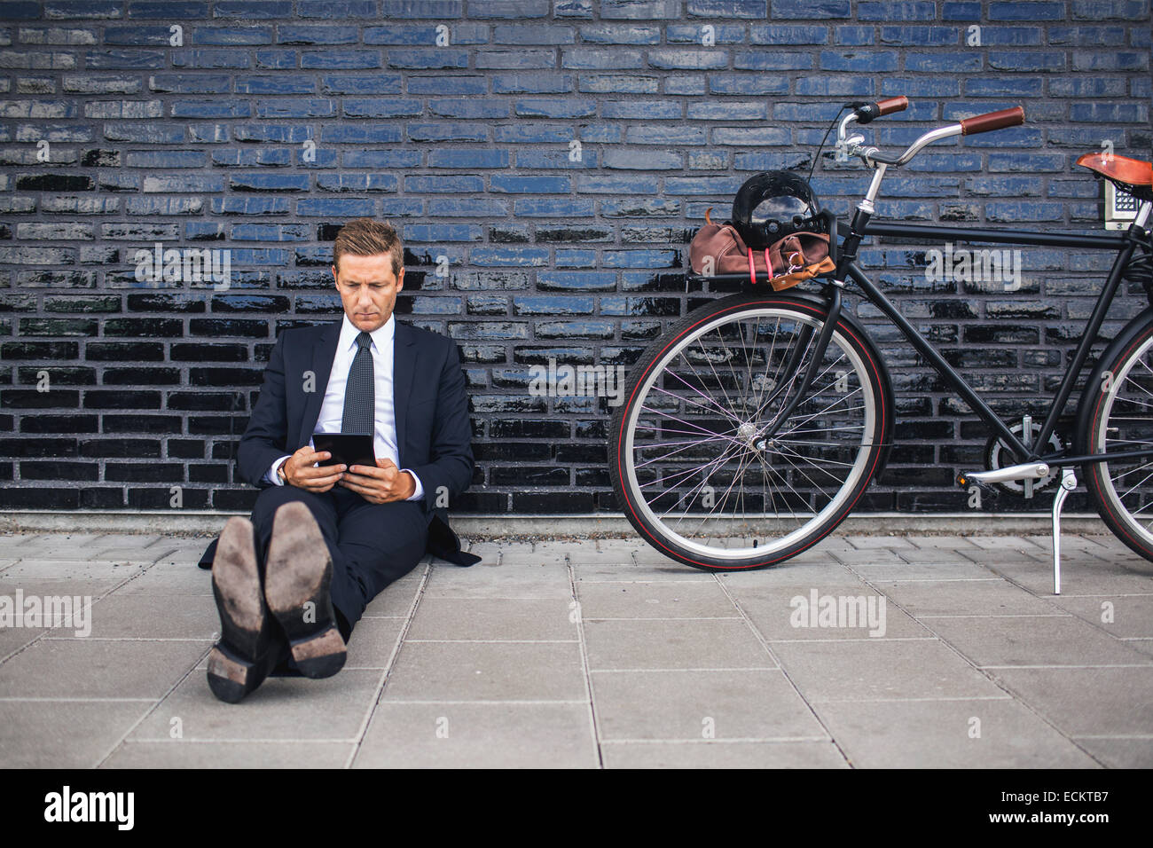 Lunghezza completa di imprenditore con tavoletta digitale mentre è seduto sul marciapiede in bicicletta Foto Stock