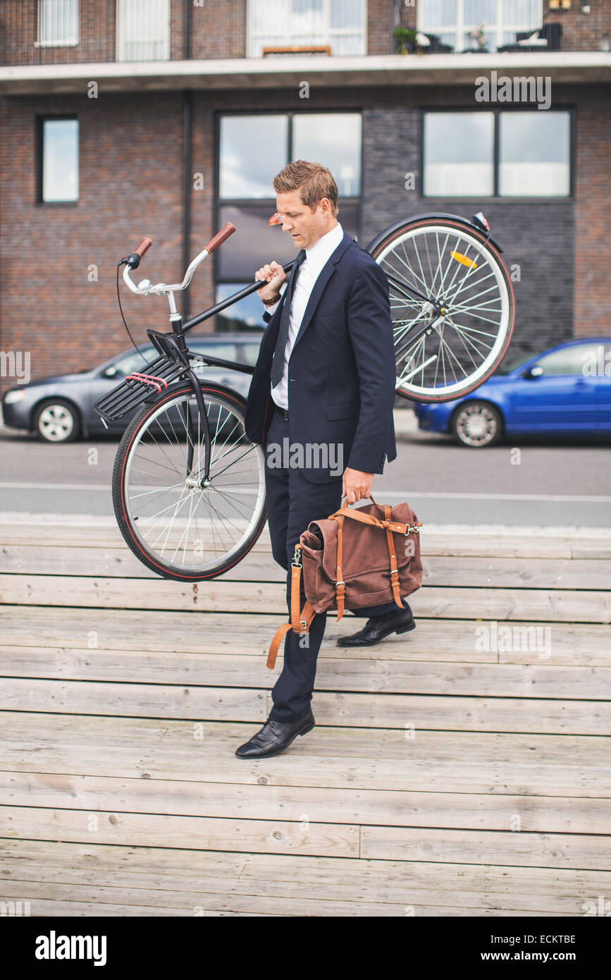 Lunghezza completa di imprenditore che trasportano biciclette mentre camminare sui passi Foto Stock