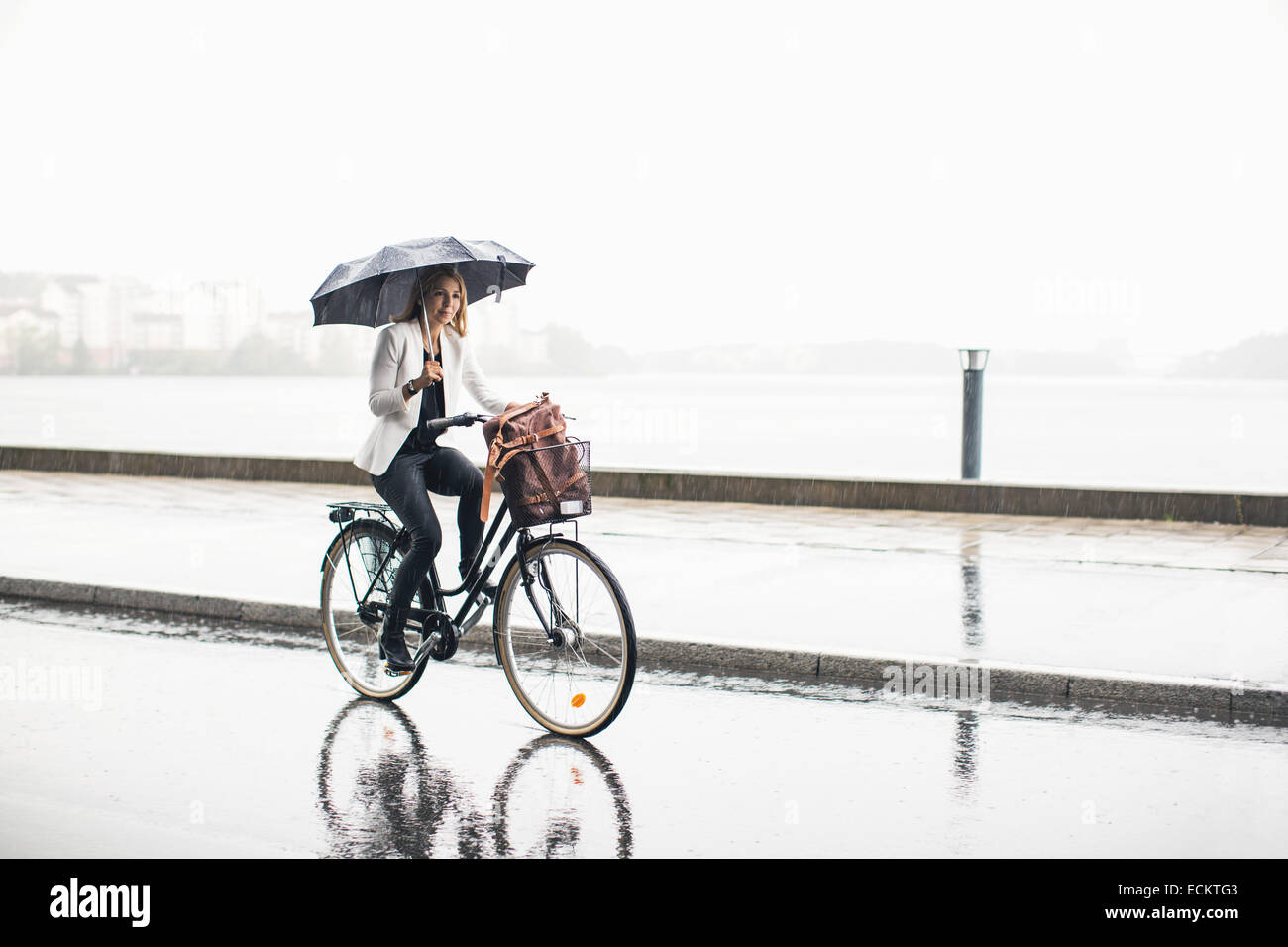 Lunghezza completa di imprenditrice Bicicletta Equitazione su bagnato via della città durante la stagione delle piogge Foto Stock