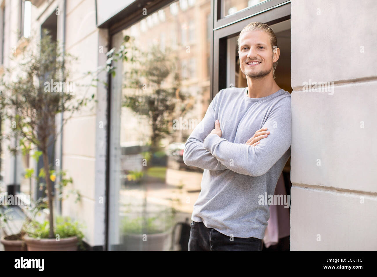 Ritratto del proprietario sorridente appoggiato sulla parete mentre in piedi al di fuori del negozio di abbigliamento Foto Stock