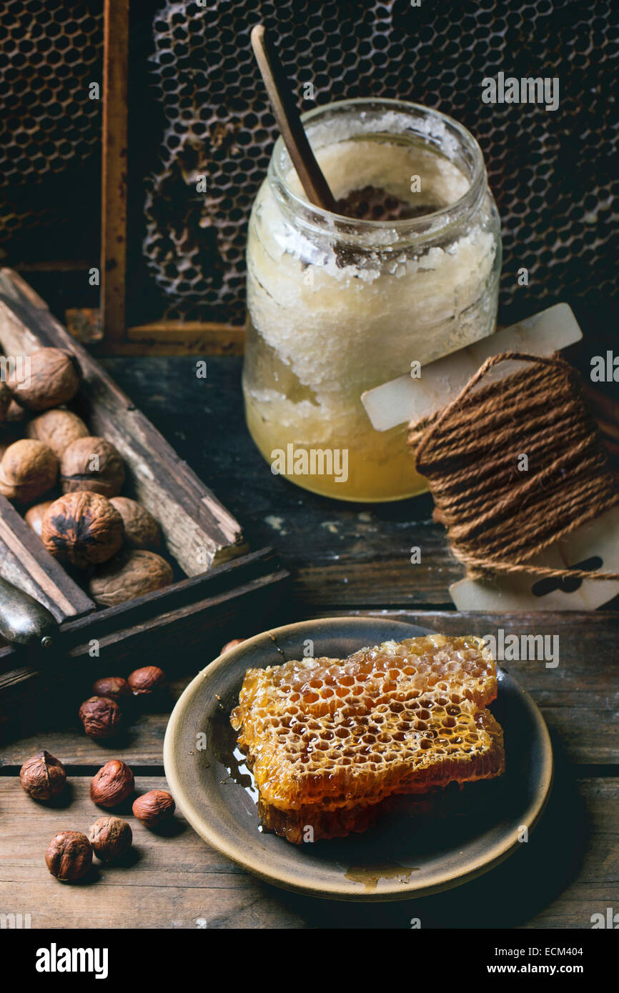 Nido fresco con un vasetto di miele vecchio e il mix di dadi su un vecchio tavolo di legno. Foto Stock