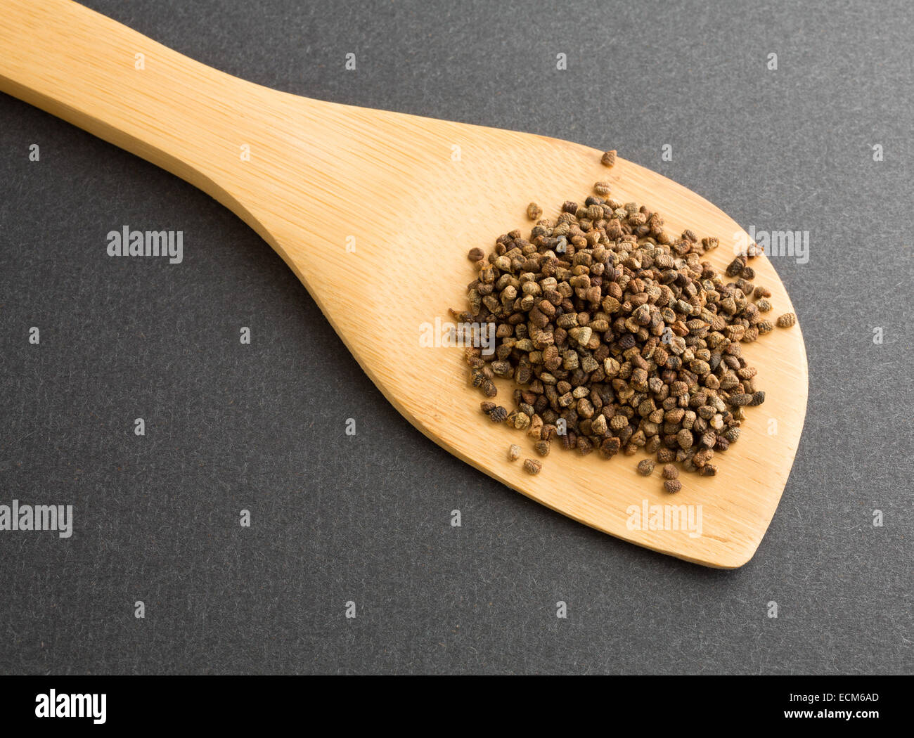 Un cucchiaio di legno con una porzione di semi di cardamomo su uno sfondo scuro. Foto Stock
