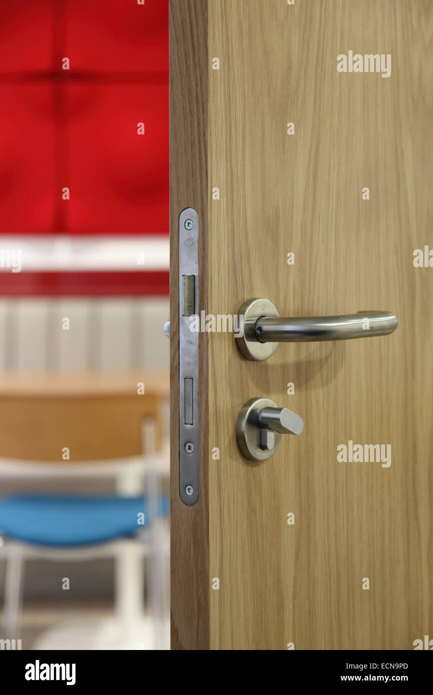 Un parzialmente aperta, moderna e oak-finitura della porta interna che mostra la maniglia della porta, serratura e meccanismo e commerciale al di là degli interni Foto Stock