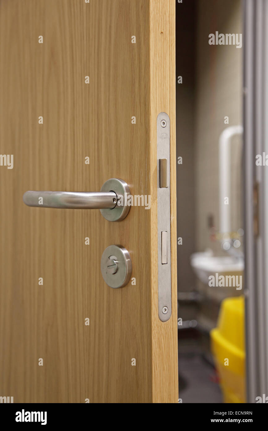 Un parzialmente aperta, moderna e oak-finitura della porta interna che mostra la maniglia della porta, serratura e meccanismo e bagno per disabili al di là Foto Stock