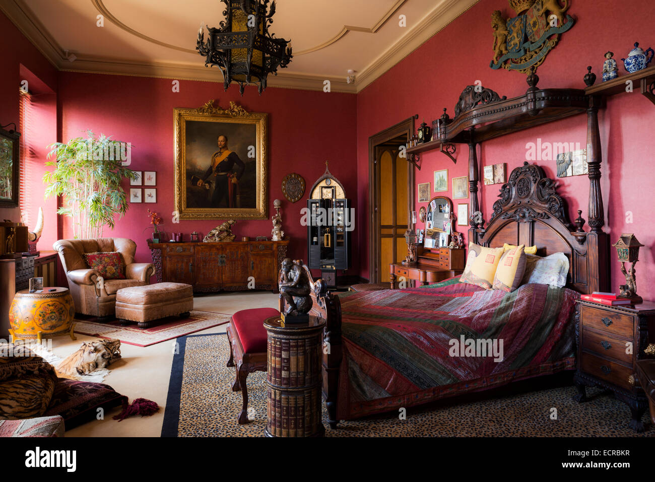 Ornati letto intagliato con coronet in grande camera rossa con leopard print moquette, montato a parete stemma e mobili antichi Foto Stock