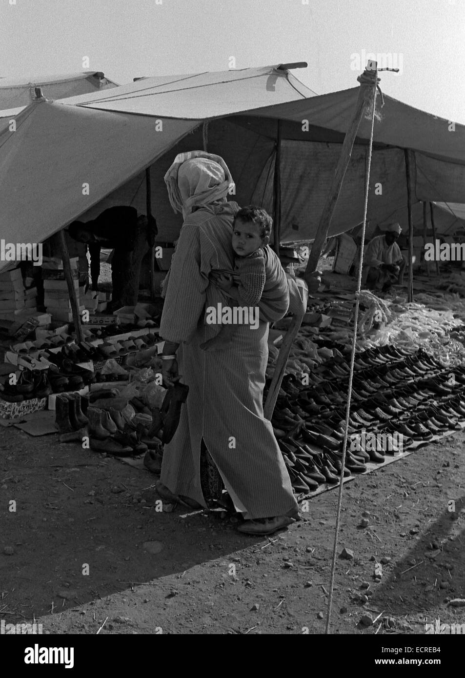 Medio Atlante, Marocco - Luglio 1979: una donna che porta il suo bambino sulla schiena, dopo aver acquistato le scarpe in un mercato Berbero in luglio, Foto Stock