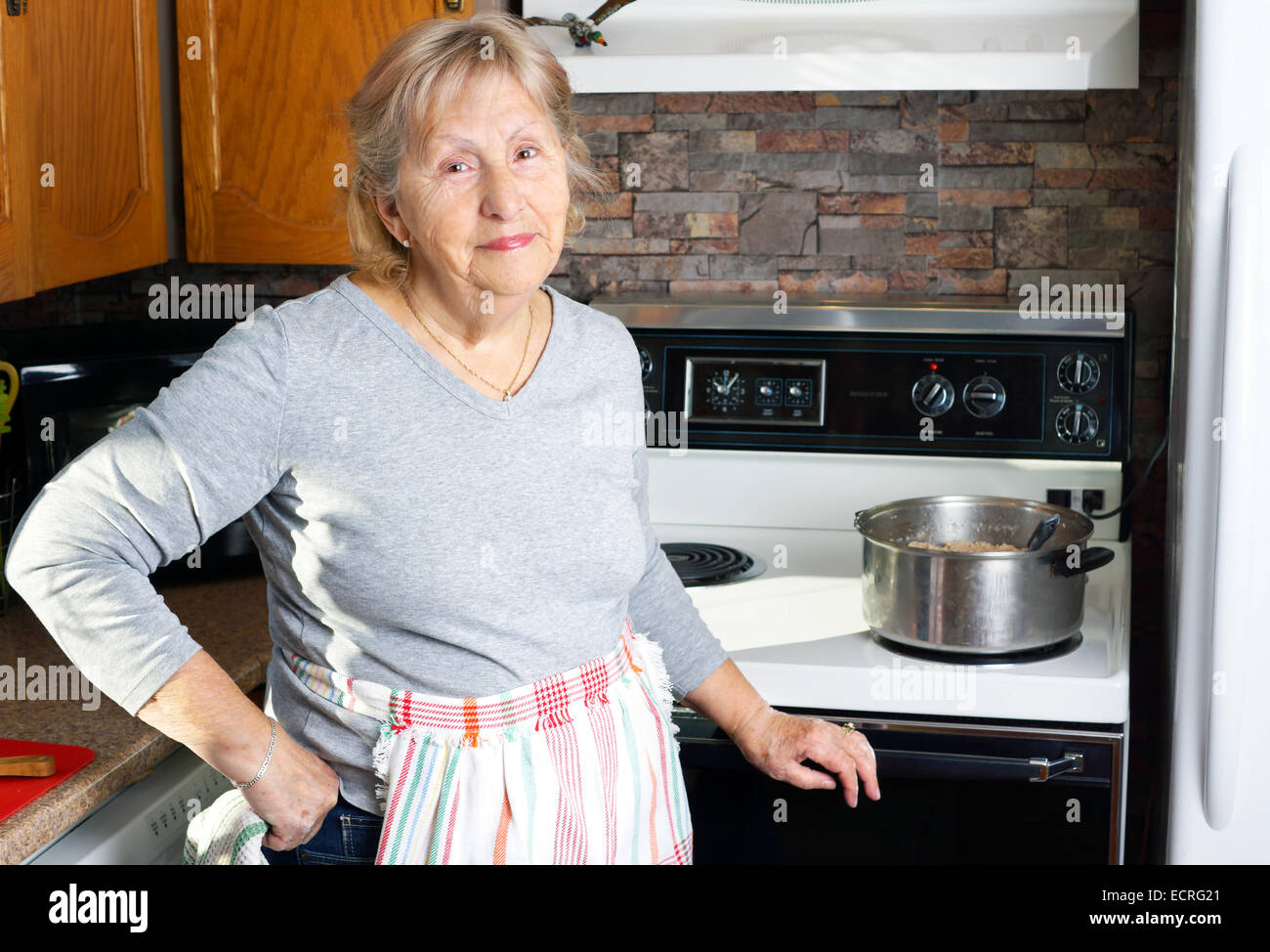 Gentile nonna sorridente o senior donna la cottura nella sua cucina Foto Stock