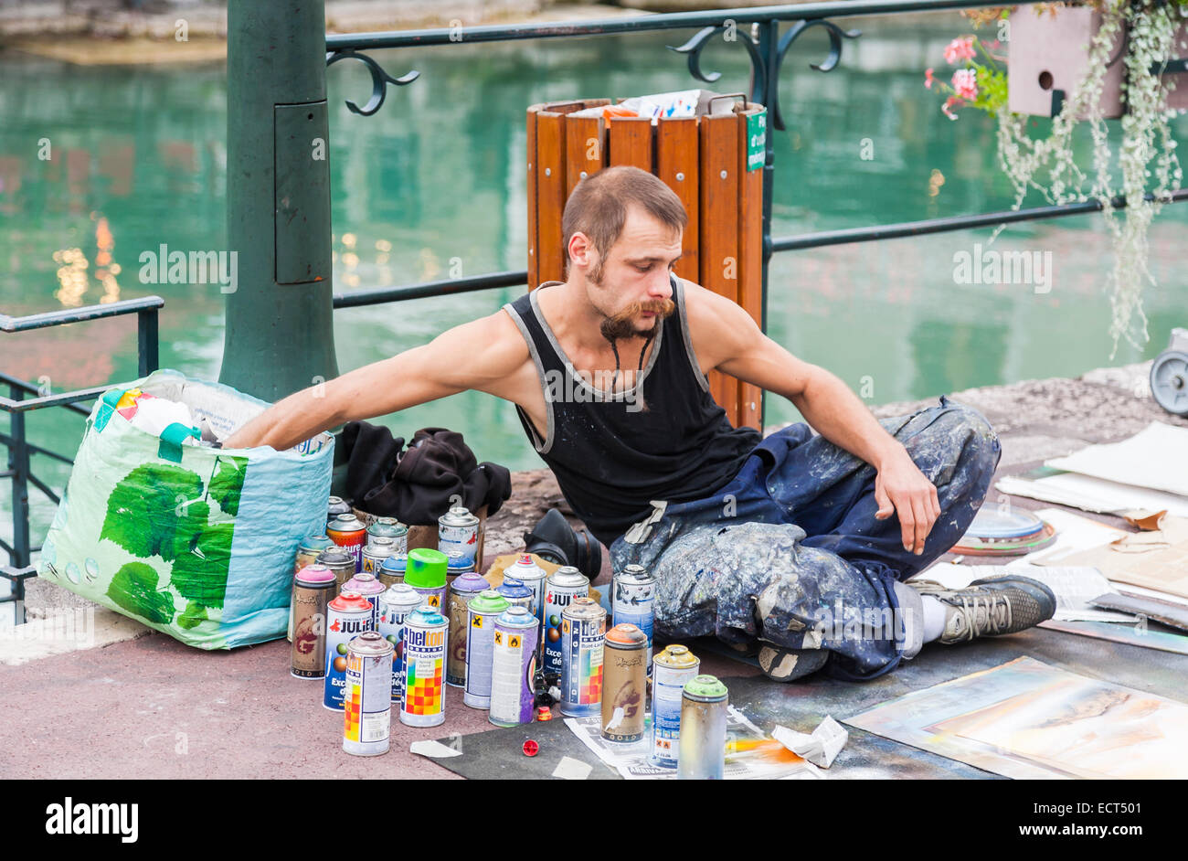 Stile di vita: Artista di strada francese locale che vende quadri dipinti a spruzzo per souvenir turistici sul marciapiede vicino al fiume Thiou ad Annecy, Francia Foto Stock
