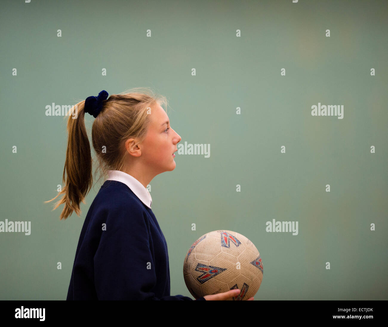 Scuola secondaria educazione fisica Wales UK: una ragazza adolescente in profilo a giocare una palla di gioco netball basket tenendo una palla in palestra, i suoi capelli in una coda di cavallo Foto Stock