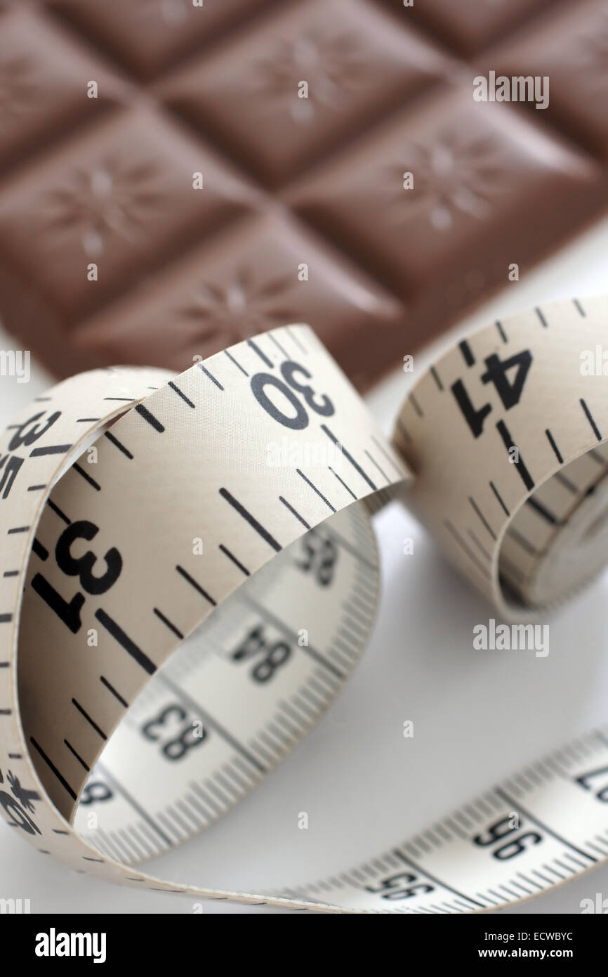 Una misura di nastro con una defocussed barra di cioccolato nel retro di un terreno alle prese con la dieta tempatation concept Foto Stock Una misura di nastro con una defocussed barra di cioccolato nel retro di un terreno alle prese con la dieta tempatation concept Foto Stock