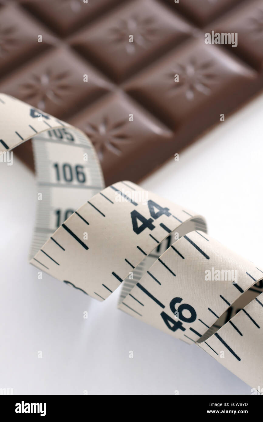 Una misura di nastro con una defocussed barra di cioccolato nel retro di massa. Il simbolo di diete e di tentazione. Foto Stock Una misura di nastro con una defocussed barra di cioccolato nel retro di massa. Il simbolo di diete e di tentazione. Foto Stock
