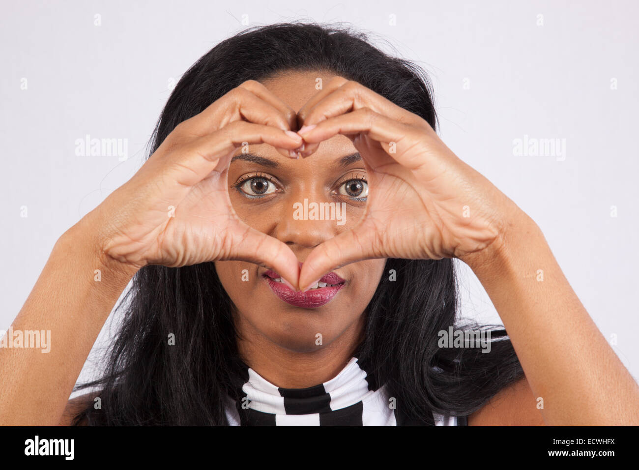 Piuttosto Nero donna seduta con un sorriso soddisfatto e facendo un cuore con le mani Foto Stock