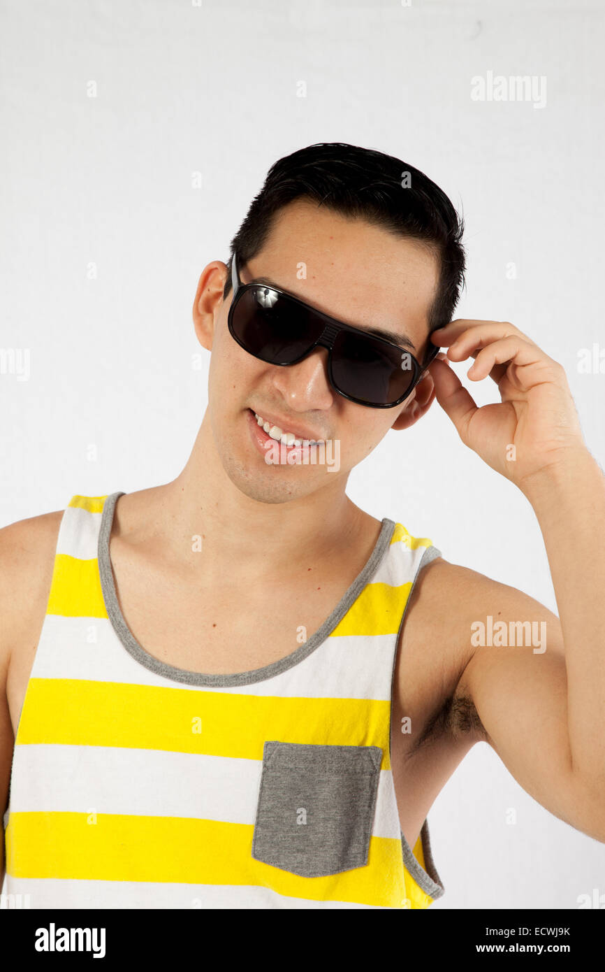 Bel uomo ispanico in giallo e bianco spogliato tank top, cercando felice con occhiali da sole Foto Stock