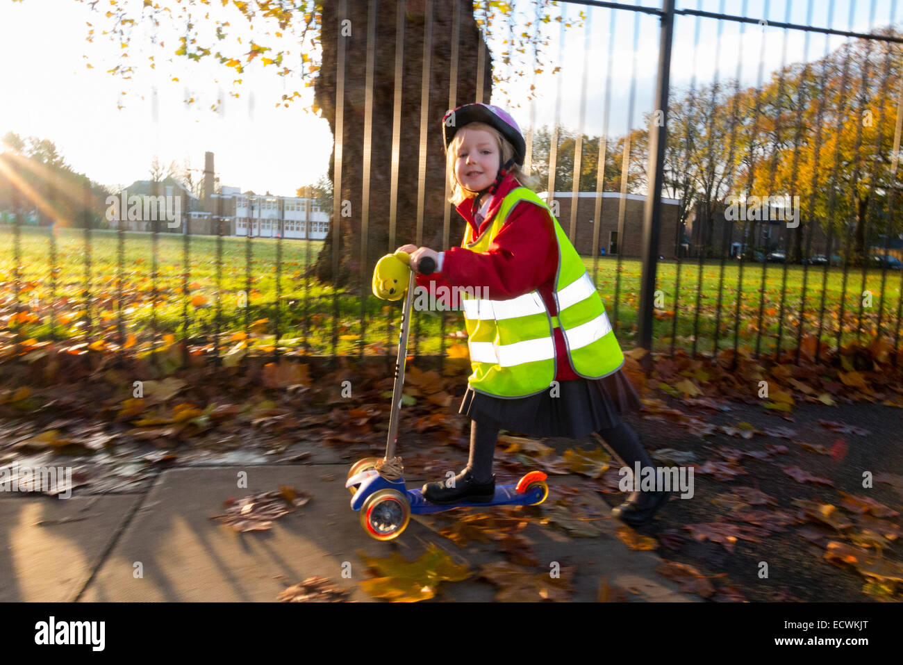 Bambino / ragazza di scooter in hi vis / alta visibilità giacca giubbotto di scootering / andando alla classe di ricezione su uno scooter a sunrise UK Foto Stock